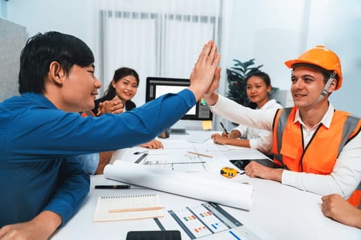 Diverse group of civil engineer and client celebrate and high five after make successful agreement on architectural project, reviewing construction plan and building blueprint at meeting table.Prudent