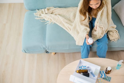 Sick ill young woman cold she covered blanket hold pills bottle read medicine prescription label, female checking ingredient information on sofa at house, pharmacy health care medicament concept