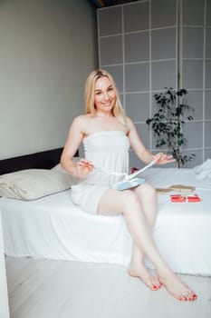 blonde woman opens holiday gift in bedroom in bed