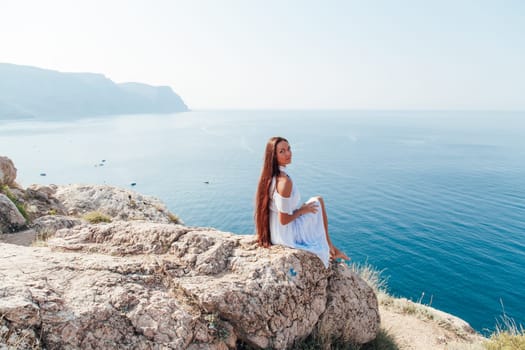 Beautiful woman in dress looks at the ocean view from the cliff