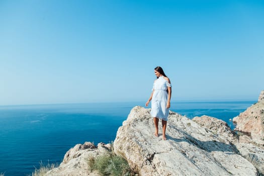 Beautiful woman in dress looks at the ocean view from the cliff
