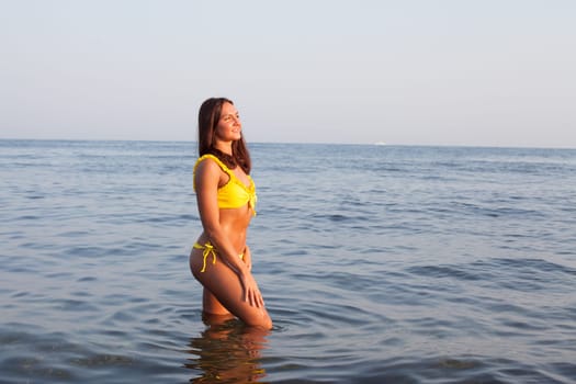 tanned woman in yellow swimsuit stands in the sea bathing on the beach