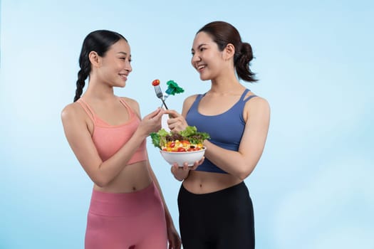 Two young sporty Asian women in sportswear holding salad bowl fill with fruit and vegetable. Natural youthful and fit body lifestyle people with balance nutrition on isolated background. Vigorous