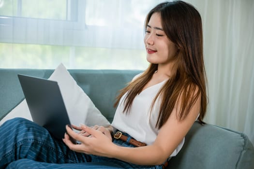 Happy woman browsing through the internet during free time on laptop computer, Female smiling sit on sofa using laptop in living room at home, girl shopping or chatting online in social media network