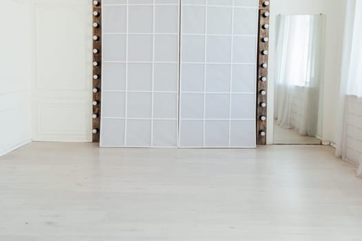 interior of an empty white room with a mirror and light bulbs
