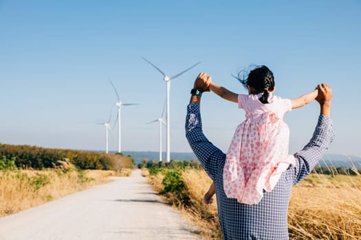 Happy father carries daughter exploring a wind farm. Family bonding by turbines symbolizes innovation in renewable energy. A joyful father-daughter moment in the windmill industry. father day concept