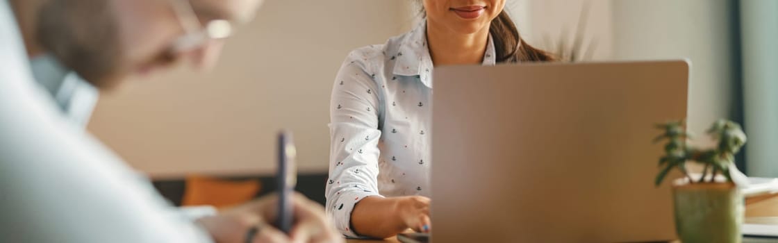 Two coworkers working together on project while using laptop in office meeting room