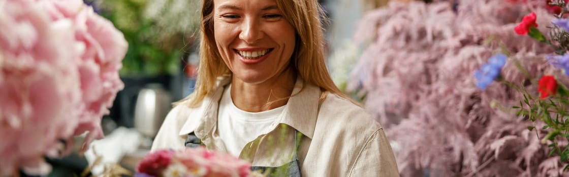 Woman florist smiling and looking on beautiful flowers composition in flower shop ready to sale