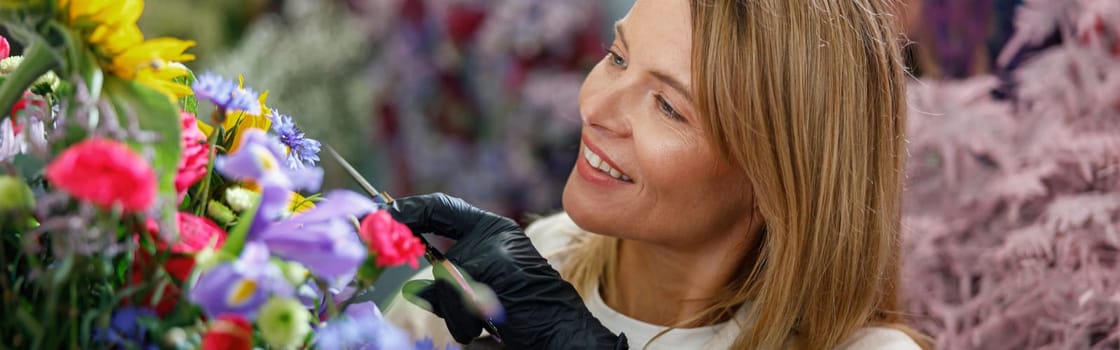 Woman florist smiling and looking on beautiful flowers composition in flower shop ready to sale