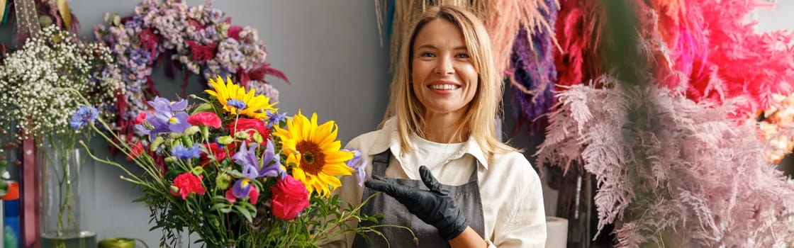 Woman florist smiling and holding beautiful flowers composition in flower shop ready to sale