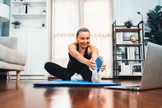 Active and fit senior woman warmup and stretching before home exercising routine at living room while watching online fitness video. Healthy lifestyle concept after retirement for pensioner. Clout