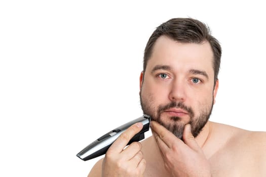 A young man with casual clothing is using an electric shaver to groom and shave his well-maintained beard. The image showcases personal grooming and hygiene against a clean white background.