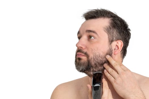 Handsome young man using an electric razor to shave his facial hair. The man is focused and intent as he grooms himself against a clean white background.