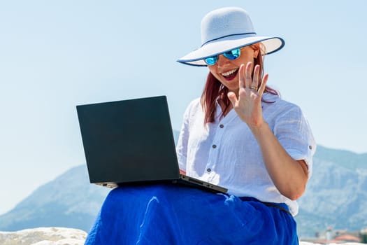 A woman employee is engrossed in her tasks on the laptop amidst the tranquil seaside environment, skillfully juggling work and vacation time for a refreshing break.