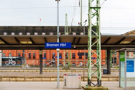 Busy morning at Bremen Central Railway Station as passengers wait for their trains on the platforms, with modern architecture and clear signage visible in the background.
