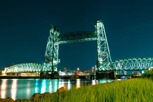 A captivating long exposure night photograph of the Koninginnebrug bridge in Rotterdam, showcasing the illuminated urban city skyline and mesmerizing light trails streaking across the waterway.