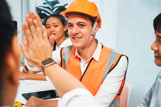 Diverse group of civil engineer and client celebrate and high five after make successful agreement on architectural project, reviewing construction plan and building blueprint at meeting table.Prudent