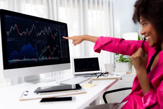 African woman blogger smiling on happy face, pointing on screen with valued stock market achievement at high profit. Concept of exchange investment online in trading application on pc. Tastemaker.