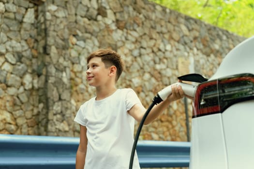 Little boy recharging eco-friendly electric car from EV charging station. EV car road trip travel concept for alternative transportation powered by clean renewable and sustainable energy. Perpetual