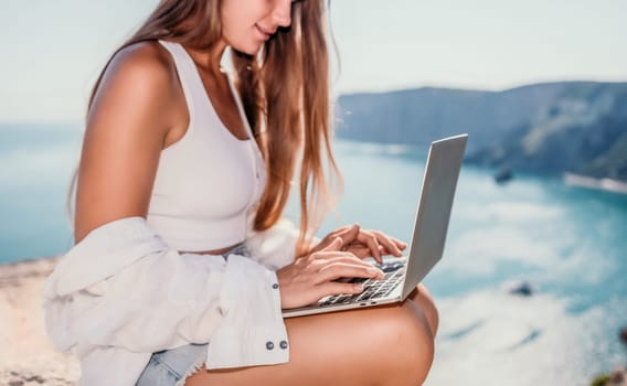 Digital nomad, Business woman working on laptop by the sea. Pretty lady typing on computer by the sea at sunset, makes a business transaction online from a distance. Freelance remote work on vacation