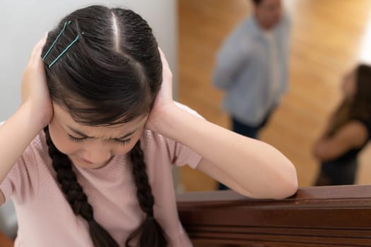 Stressed and unhappy young girl cover her ears blocking sound tension by her parent argument from the stair. Unhealthy family and domestic violence lead to traumatic childhood and anxiety. Synchronos