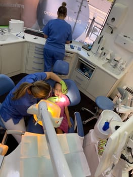 Dentist examining a little girl sitting with her mouth open in a dental chair. High quality photo