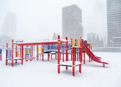 Children's play ground in snow with high-rise buildings on the background. Winter season in British Columbia, Canada.