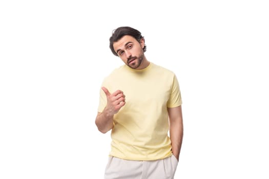 young brutal brunette man in a T-shirt points his hand to the side on a white background with copy space.