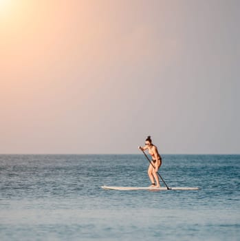 Sea woman sup. Silhouette of happy middle aged woman in rainbow bikini, surfing on SUP board, confident paddling through water surface. Idyllic sunset. Active lifestyle at sea or river