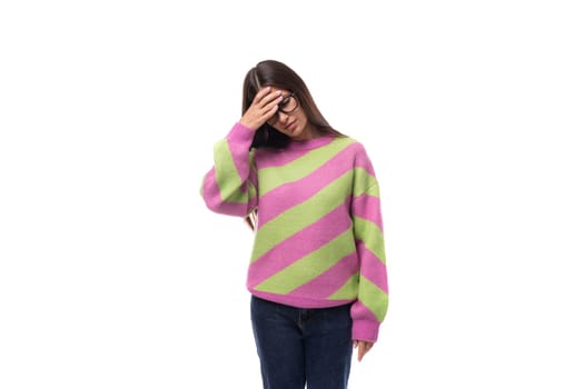 young upset caucasian woman with black hair in glasses dressed in a pink striped sweater.