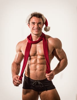Christmas season: muscular bodybuilder shirtless wearing Santa Claus red hat, on white