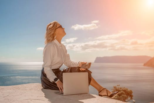 Freelance women sea. She is working on the computer. Good looking middle aged woman typing on a laptop keyboard outdoors with a beautiful sea view. The concept of remote work