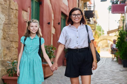 Outdoor portrait of mom and child daughter 10, 11 years old on street of old city. Mother and preteen schoolgirl holding hands walking together. Parent child relationship, lifestyle people
