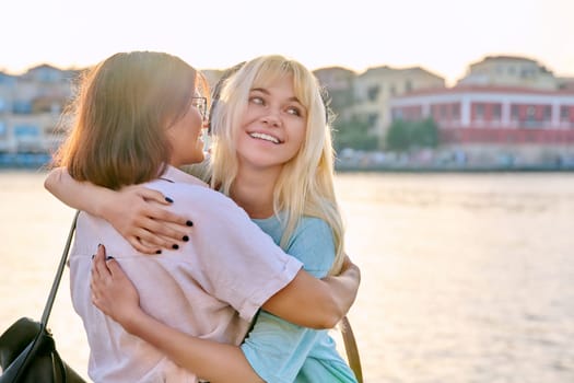 Happy mom and teenage daughter hugging together. Family mother and daughter outdoor, on sunset summer sea embankment. Mother's day, childhood, friendship, love, parent teenager concept