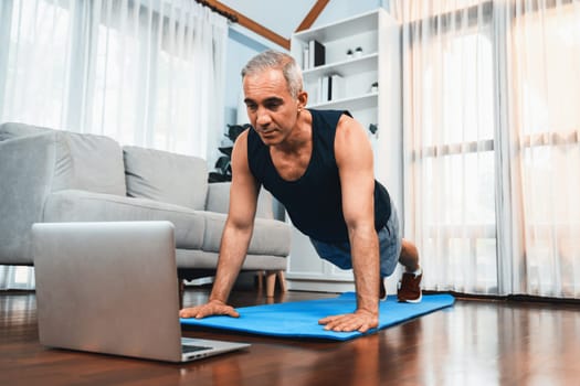 Athletic and sporty senior man doing pushup on exercising mat while watching instruction from online video at home exercise as concept of healthy fit body lifestyle after retirement. Clout