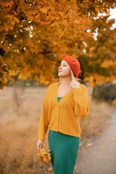 autumn woman in a red beret, yellow sweater and green skirt, against the background of an autumn tree.
