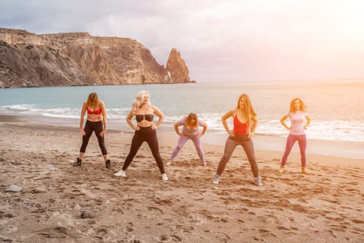 A group of five female friends are doing exercises on the beach. Beach holiday concept, healthy lifestyle.