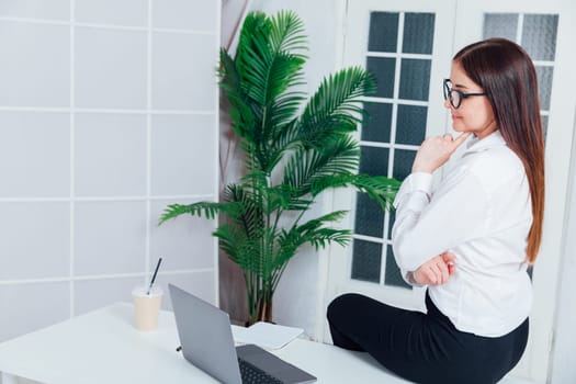 female gardener in glasses using laptop, communicates on internet with customer in home