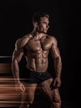 A Strong Display of Masculinity: Flexing Muscles and Striking a Pose in Studio. A man posing for a picture while flexing his muscles in dramatic lights in studio