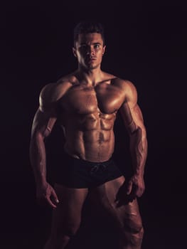 A Strong Display of Masculinity: Flexing Muscles and Striking a Pose in Studio. A man posing for a picture while flexing his muscles in dramatic lights in studio