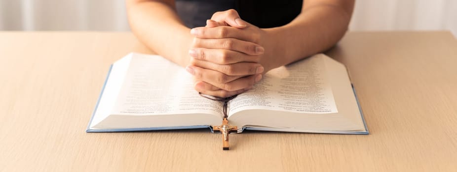 Cropped image of praying male hand holding cross on holy bible book at wooden table. Top view. Concept of hope, religion, faith, christianity and god blessing. Warm and brown background Burgeoning.