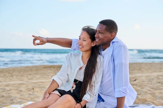 Outdoor portrait of happy young couple on sandy beach. Multicultural couple, Asian woman African American man enjoying sea nature, relationship, vacation together. Seaside resort travel tourism people