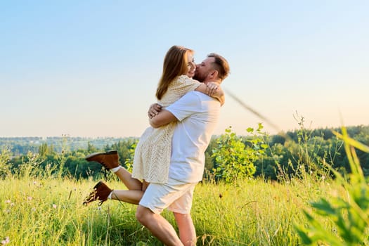 Happy middle-aged couple having fun on a summer meadow. 40 year old man and woman embracing, enjoying, celebrating, laughing. Holiday, nature, date, love, romance, relationship, joy concept