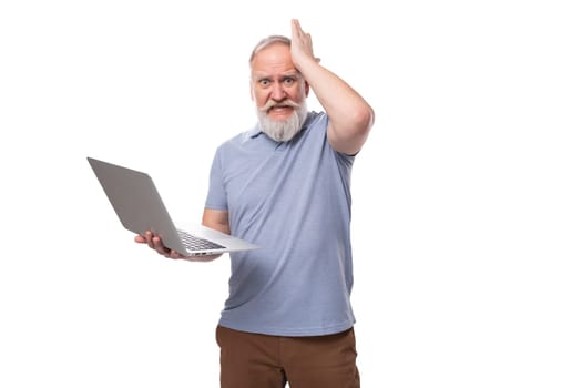 stylish pensioner man with beard and mustache in shirt and trousers holding laptop and working remotely.