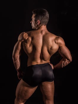 Handsome bodybuilder man's back, doing classic pose, looking away, on dark background