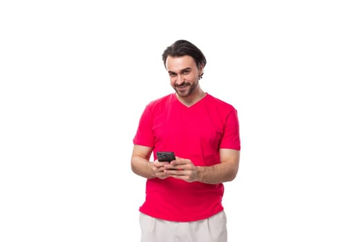 young joyful man dressed in a red t-shirt smiling holding a phone in his hand.