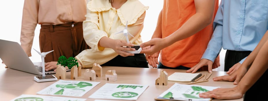 Windmill model represented using renewable energy placed during presenting green business on table with wooden block and environmental document scatter around. Closeup. Delineation.