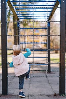 Little girl is climbing the chain ladder in the playground. Back view. High quality photo