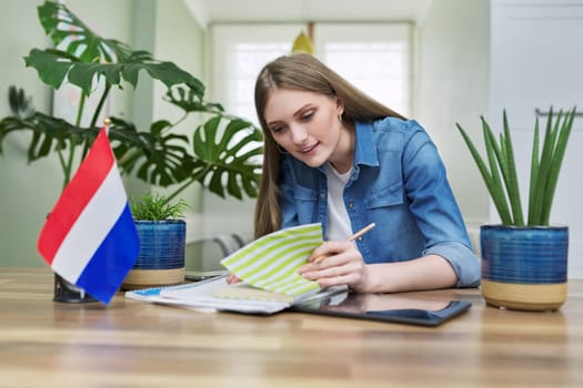 Young female student looking at webcam talking studying or teaching. On table textbooks, flag of Netherlands. Education, university, online learning, remote distant lessons, knowledge people concept