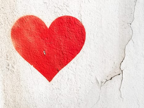 Red love heart spray painted on wall background. One red heart painted on concrete fence backdrop. Happy Valentines day. 14th february.